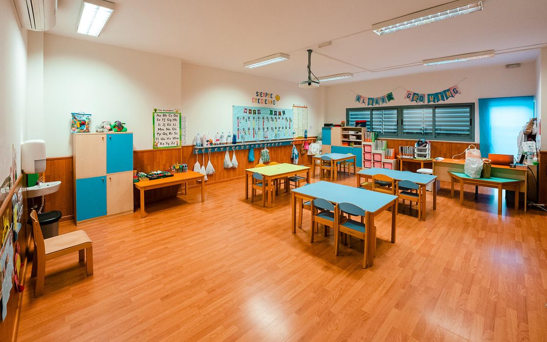 Aula de Infantil con mesas bajas de colores y suelo de madera
