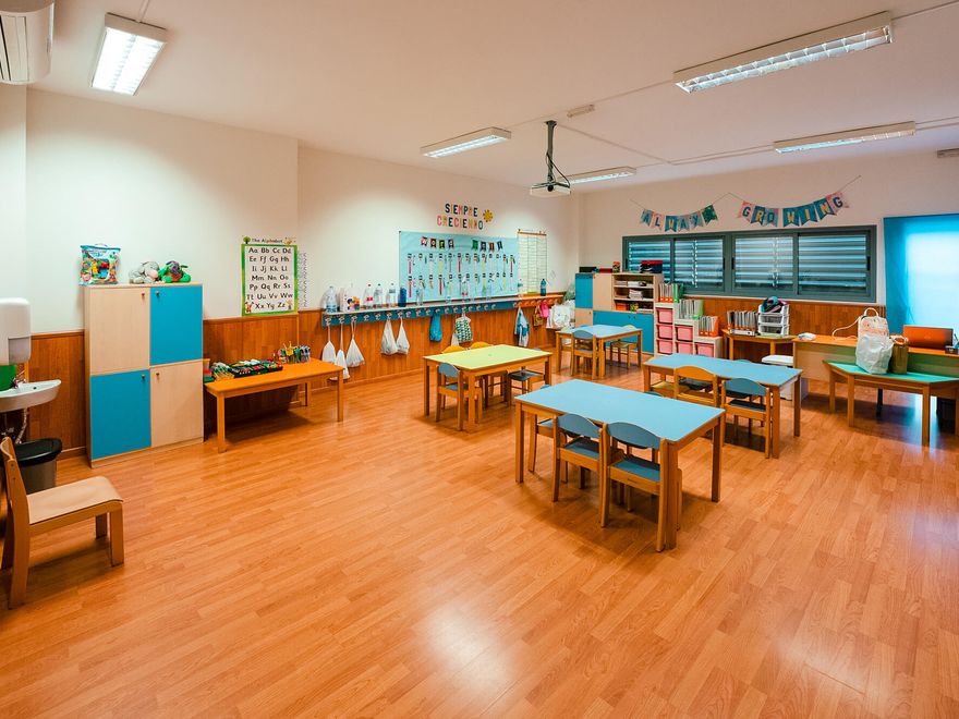 Aula de Infantil con mesas bajas de colores y suelo de madera