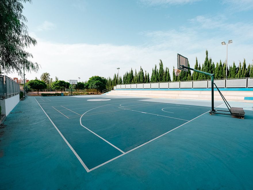 Pista de baloncesto exterior con gradas, rodeada de cipreses
