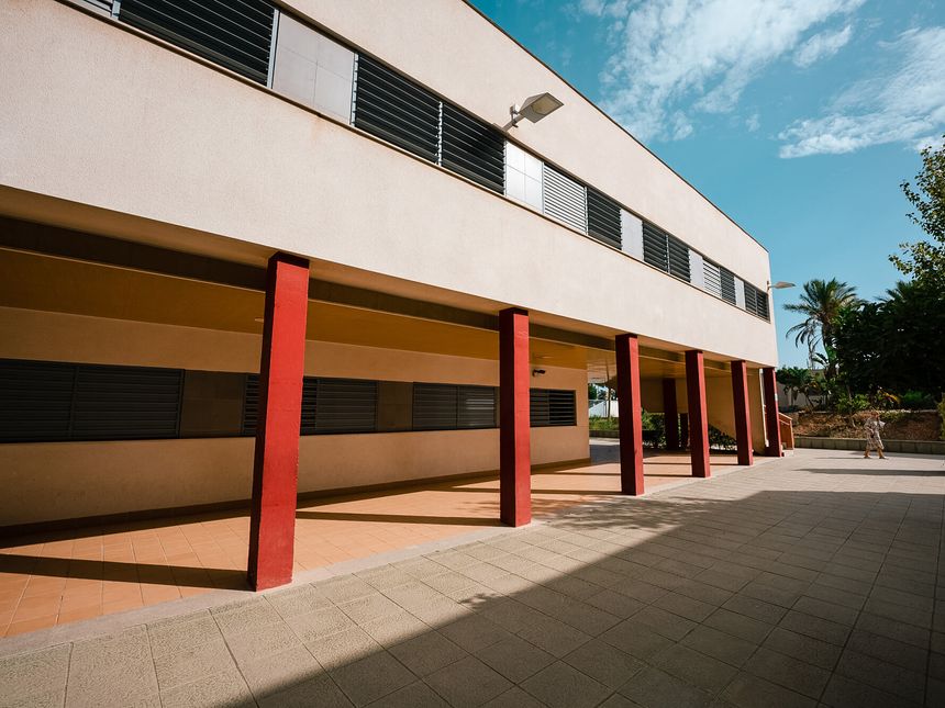 Porche con pilares rojos junto a un edificio del colegio