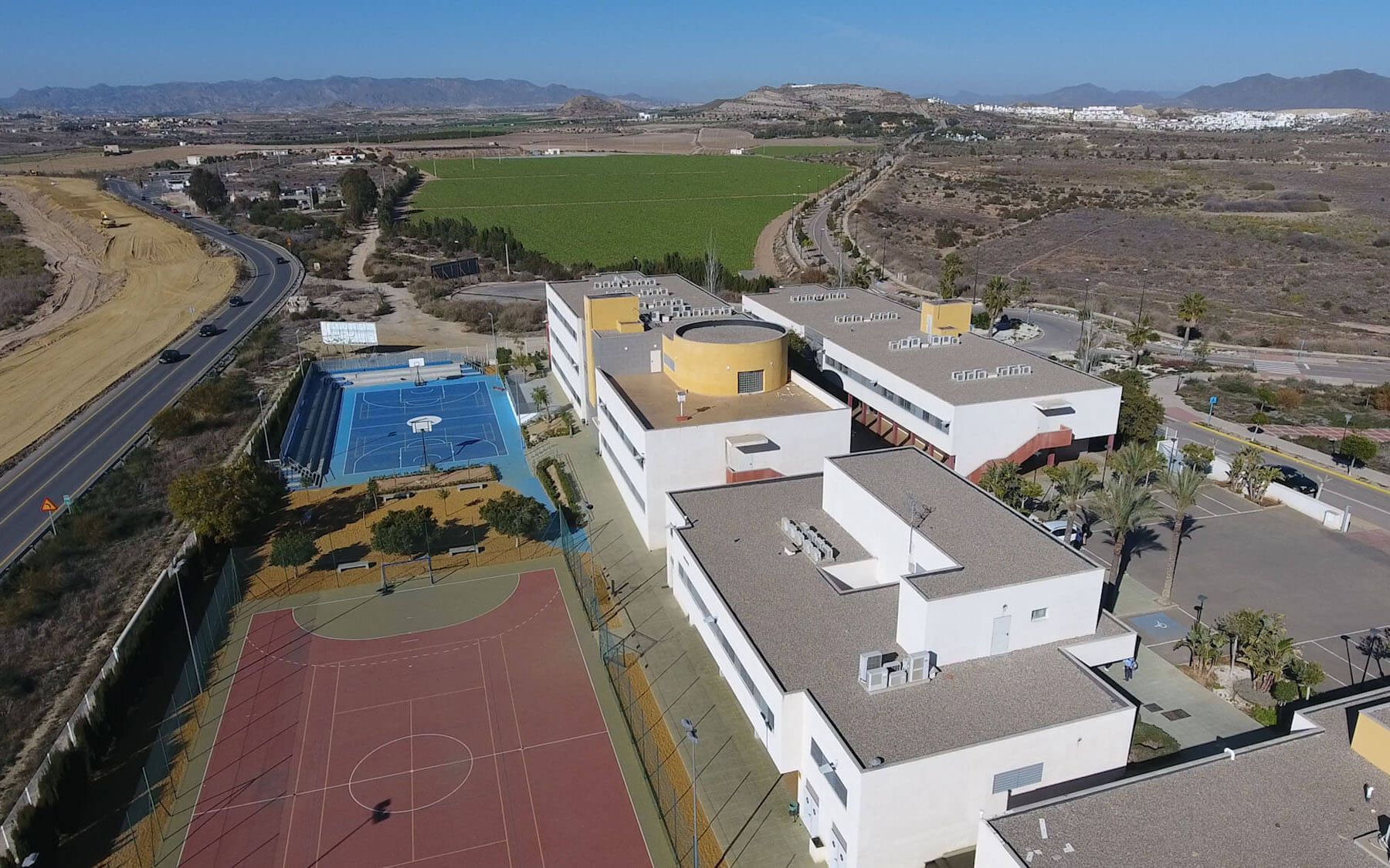 Vista aérea del colegio: edificios blancos, pistas deportivas y, al fondo, la sierra