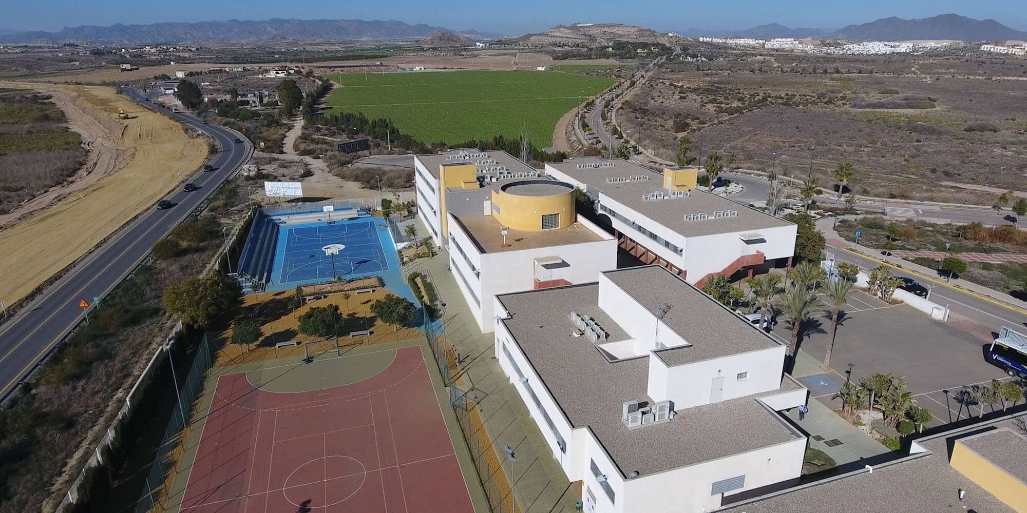 Vista aérea del colegio: edificios blancos, pistas deportivas y, al fondo, la sierra