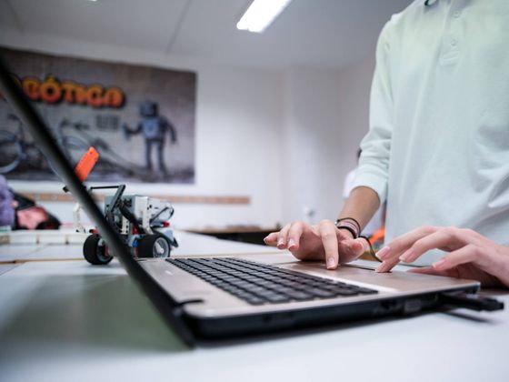 Unas manos programan en un portátil junto a un robot construido con piezas LEGO