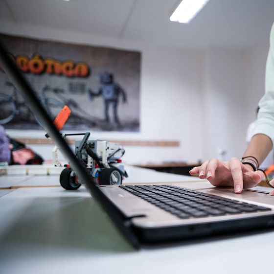 Unas manos programan en un portátil junto a un robot construido con piezas LEGO