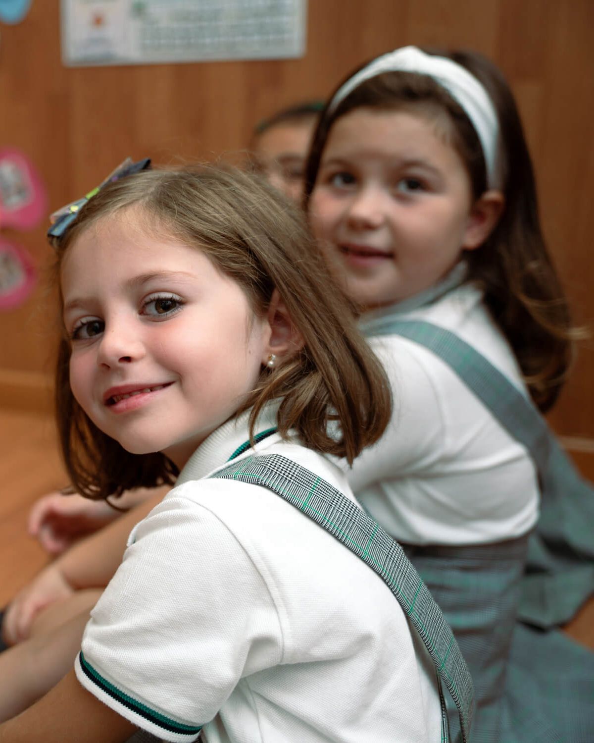 Dos alumnas con el uniforme de ValdeSerra sonríen sentadas en el suelo del aula